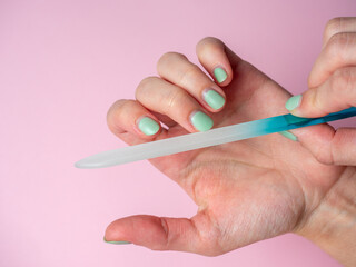 A woman uses a nail file to put her nails in order on a paper pink background. Nail care at home