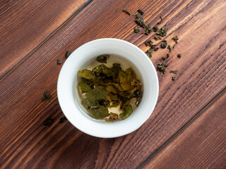 green tea is brewed in a white bowl on a wooden background. Dry tea leaves lie nearby. Top view