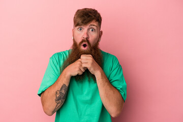 Young caucasian ginger man with long beard isolated on pink background praying for luck, amazed and opening mouth looking to front.