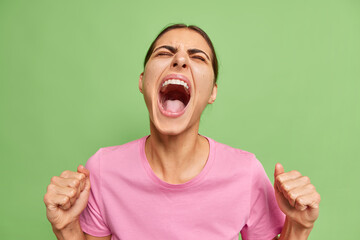 Photo of emotional young European woman yells loudly loses temper keeps fists clenched screams and...