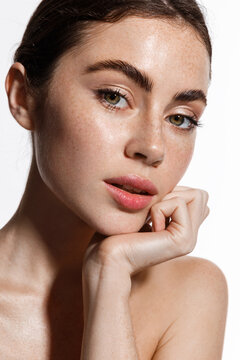 Attractive female model with natural makeup, glowing healthy skin after shower, looking sensual at camera, touching her face, showing moisturizer cream after-effect, white background