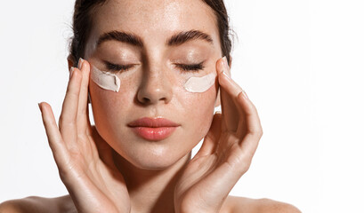 Close up beauty girl with freckles and thick eyebrows, applying moisturizing skincare cream, lotion...
