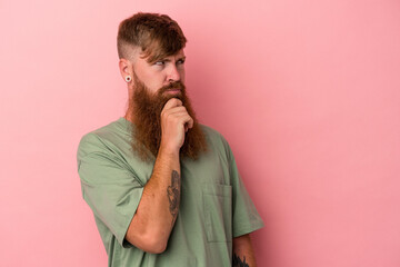 Young caucasian ginger man with long beard isolated on pink background relaxed thinking about something looking at a copy space.