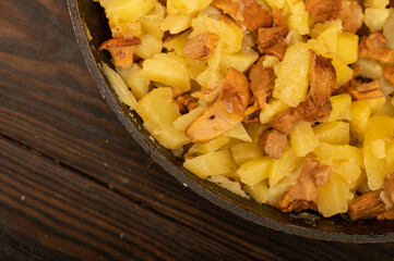 Potatoes fried in a frying pan with mushrooms on a wooden table. A traditional village dish.