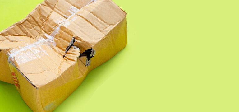 Damaged cardboard box with hole on green background.