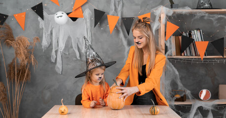 Mom and daughter make a pumpkin jack-o-lantern for Halloween. Traditional autumn witch holiday at...