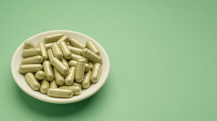 Close-up of Andrographis paniculata capsules are in a dish isolated on a green background. Space for text. Herbal, medicine, and healthcare concept