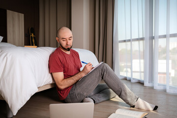 An adult bald man sits on the floor of a home and studies. The concept of online courses and online learning