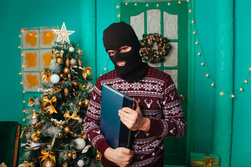 A masked bandit stole a laptop in the new year and escapes. A man in a balaclava holds a computer....