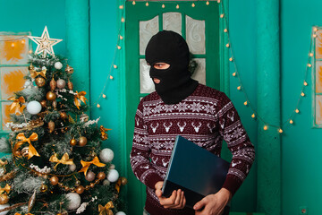 A masked bandit stole a laptop in the new year and escapes. A man in a balaclava holds a computer....