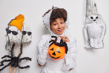 Pleased African American woman holds carved halloween jack on lantern with black spooky spider...