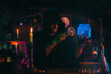 alchemist magician holds a flask with a potion in hands. Sorcerer is witcher in dark laboratory