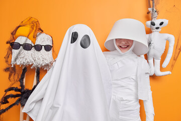 Funny positive girl wears lampshade on head ghost costume poses near halloween mummy pose indoor...
