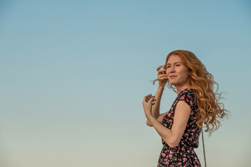 Beautiful redhead girl a summer dress against a sky. Girl looking up and aside the camera, copyspace