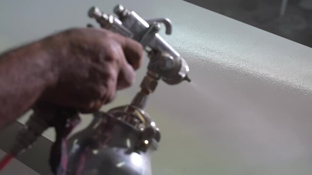 worker paints a board with a spray gun at a furniture factory