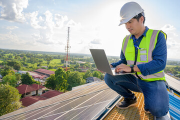 Asian technician working on a solar power plant using a laptop computer to check the maintenance of solar panels on the roof.