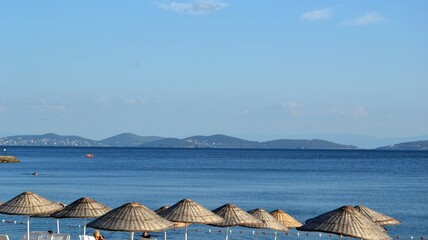 Beach straw umbrellas on coast of Marmara sea under blue sky with horizon in Istanbul during summer.