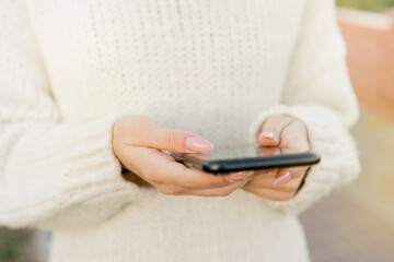 Close up image. Young girl using modern smartphone device, female hands holding mobile phone on city street.