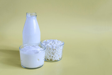 Sour cream and cottage cheese in a glass container with milk on a yellow background. Sour cream, cottage cheese and milk in a transparent dish on a light background place for text