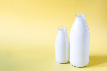 Two glass bottles of milk on a yellow background. A liter and 0.5 liters of milk in glass bottles on a colored background place for text