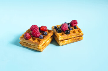 Fresh waffles with different berries of black and red color on a blue background close-up. Homemade cakes crispy waffles on a colored background	