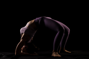 Fit girl practicing yoga in a studio. Half silhouette side lit fitness model.
