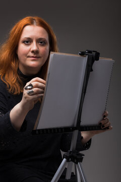 Red hair woman painting. Portrait of an artist against gray background.