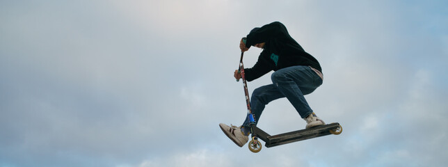 Teenager performs trick in the city skate  park. Push scooter. He is jumping. Extreme sports is popular among youth. Frontal view