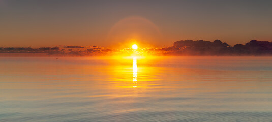 Sunrise over an unbroken sea horizon. The first sunbeams for the day reflects in the calm waters of...