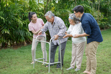 asian senior father trying walk with walker and adult son daughter wife support in gaden at home. old man disabled walking and caregiver young man helping in back yard . health care family lifestyle