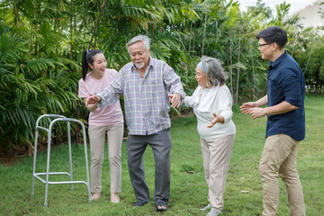 asian senior father trying walk with walker and adult son daughter wife support in gaden at home. old man disabled walking and caregiver young man helping in back yard . health care family lifestyle