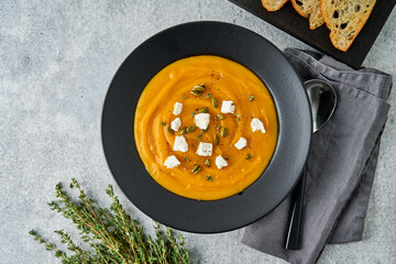 Autumn pumpkin creamy puree soup with feta cheese, thyme, seeds and crispy toast in gray plate on stone background. Traditional seasonal thanksgiving and halloween dish