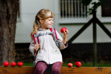 Little cute girl eat red ripe apple. Happy smiling preschool child with satchel holding fresh bio fruits. Apples from harvest.