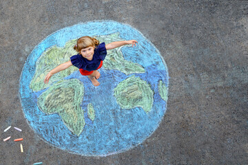 Little preschool girl with earth globe painting with colorful chalks on ground. Positive toddler...