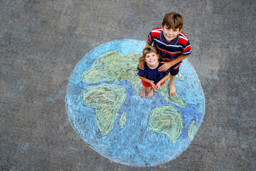 Little preschool girl and school kid boy with earth globe painting with colorful chalks on ground....