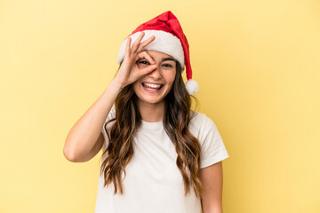 Young caucasian woman celebrating Christmas isolated on yellow background excited keeping ok gesture on eye.