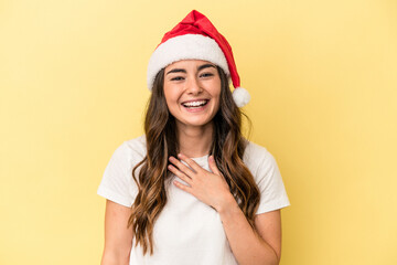 Young caucasian woman celebrating Christmas isolated on yellow background laughs out loudly keeping hand on chest.