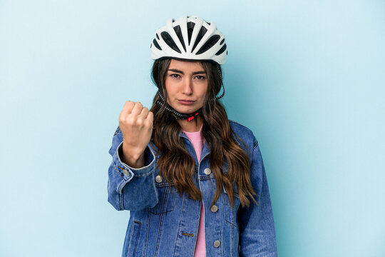 Young caucasian woman rinding a bike isolated on blue background showing fist to camera, aggressive facial expression.