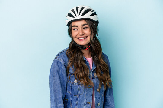 Young caucasian woman rinding a bike isolated on blue background looks aside smiling, cheerful and pleasant.