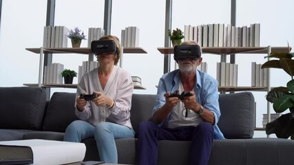 Senior mature couple having fun with virtual reality glasses, senior couple sitting on the sofa holding joysticks and laughing while playing a video game, Happy elderly technology concepts - Powered by Adobe