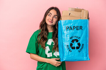 Young caucasian woman recycled paper isolated on pink background dreaming of achieving goals and...