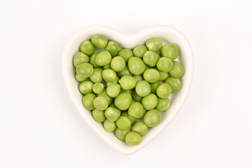 Green peas are lying in a white plate in the shape of a heart on a white background.Cultivation and care of agriculture, agronomy, breeding, vegetarianism, protein production, sports nutrition.