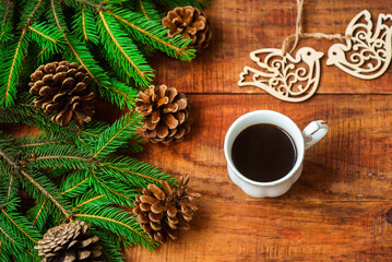 Obraz na płótnie Canvas Christmas background. Spruce branches, wooden bird figures and cup with coffee on a wooden background.