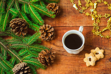 Obraz na płótnie Canvas Christmas background. Composition of spruce branches with pinecones and cup with coffee with cookies on a wooden background. Copy space Top view. Christmas or New Year's card. flat lay