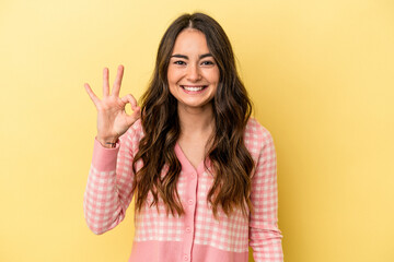 Young caucasian woman isolated on yellow background cheerful and confident showing ok gesture.