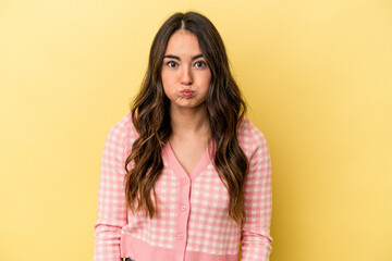 Young caucasian woman isolated on yellow background blows cheeks, has tired expression. Facial expression concept.