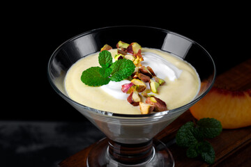 Mango dessert with yogurt topped with pistachio and mint in glass bowl against the black background. Exquisite dessert - obrazy, fototapety, plakaty