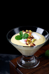 Mango dessert with yogurt topped with pistachio and mint in glass bowl against the black background. Exquisite dessert