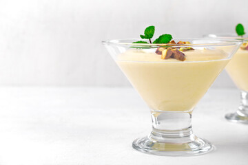 Mango dessert with yogurt topped with pistachio and mint in glass bowl on the white table. Copy space