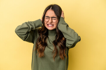 Young caucasian woman isolated on yellow background covering ears with hands.